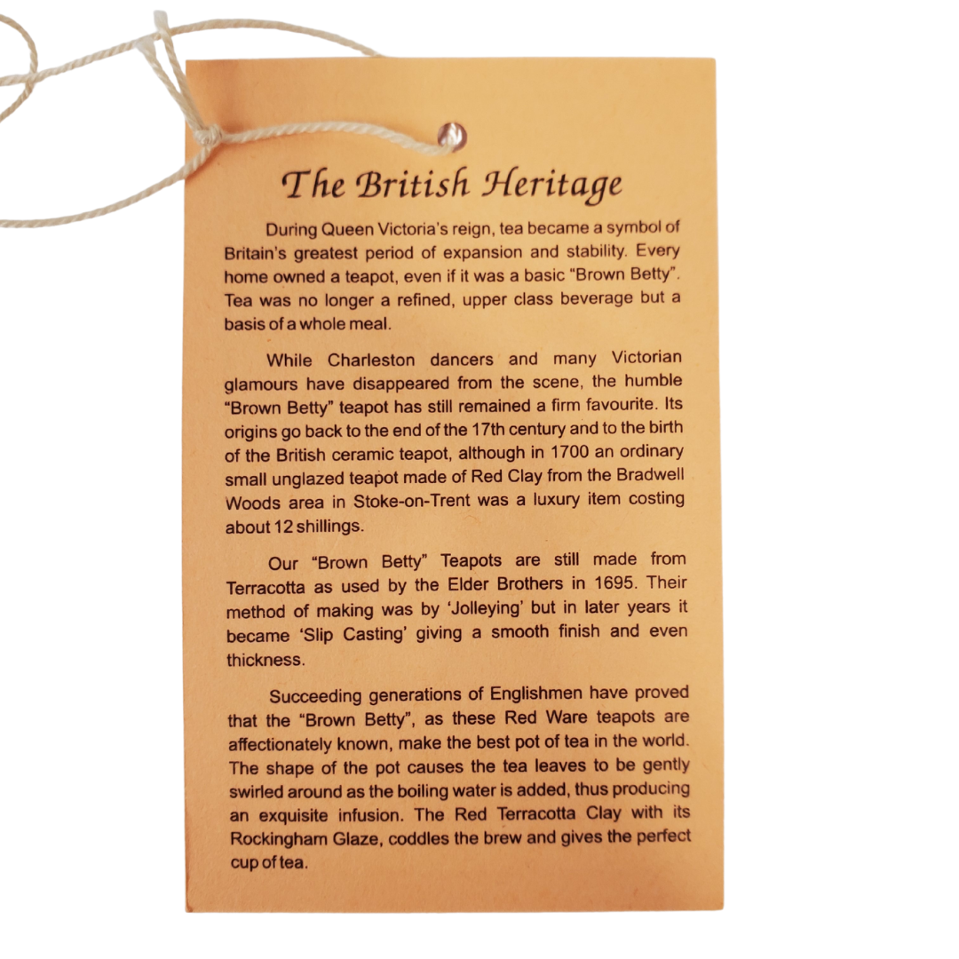 Close up  of back of Tag - During the reign of Queen Victoria, tea was a symbol of one of the greatest periods in Britain's history. Everyone owned a teapot in this era, many owning the "Brown Betty". Tea was no longer something the upper class could enjoy but became a household staple. This Brown Betty teapot is made from red terracotta and Rockingham glaze. Enjoy your perfect cup of tea without the worry of spiling with the specially designed spout. The Union Jack in the photo is a removable stick