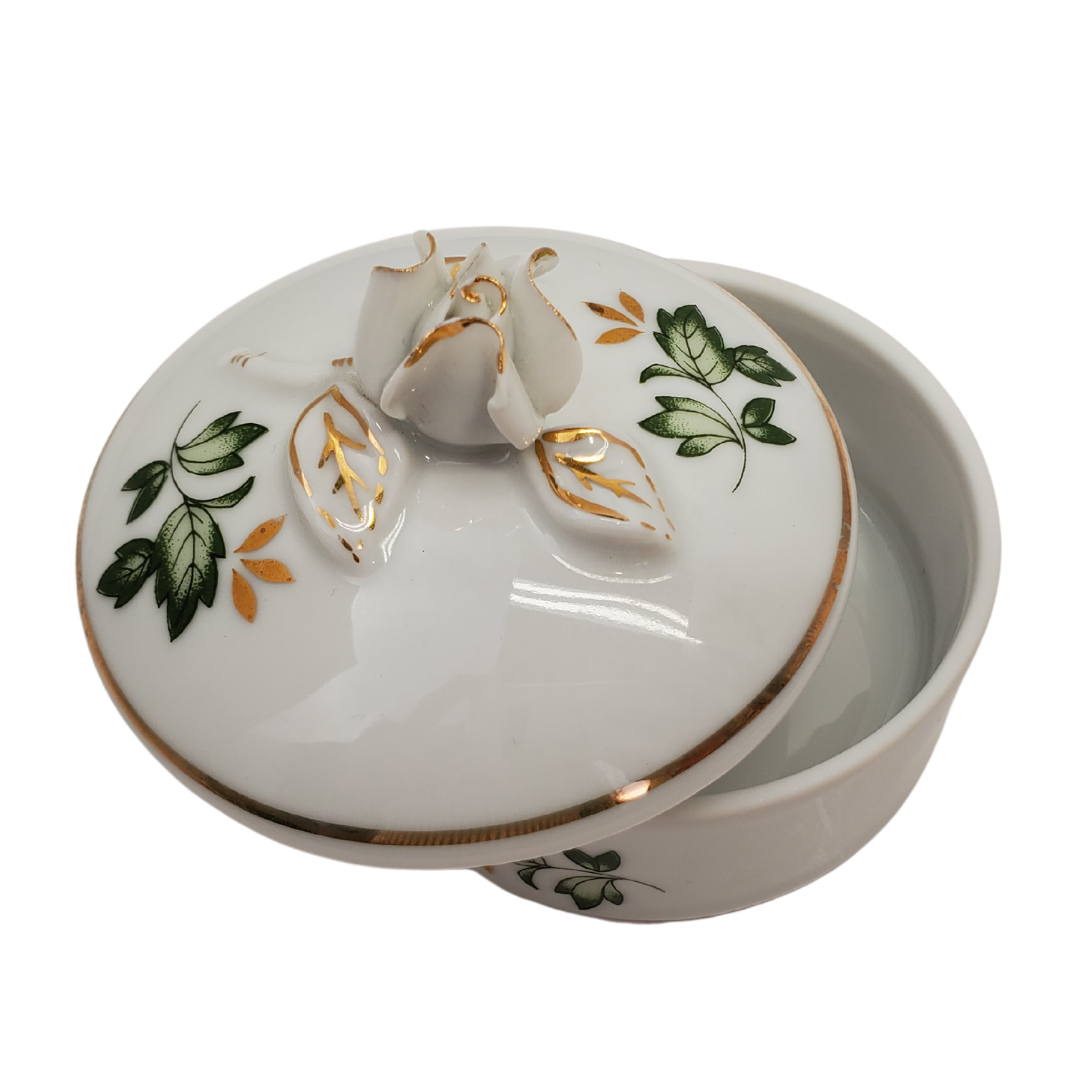 Pre-owned Hollohaza Hungary porcelain trinket box, with green leaves, gold leaves, gold trimming, and rosebud as handle. Perfect addition to your vanity or bathroom for storing cotton pads!  Measurement: Height: 2.5" Diameter: 2/75"