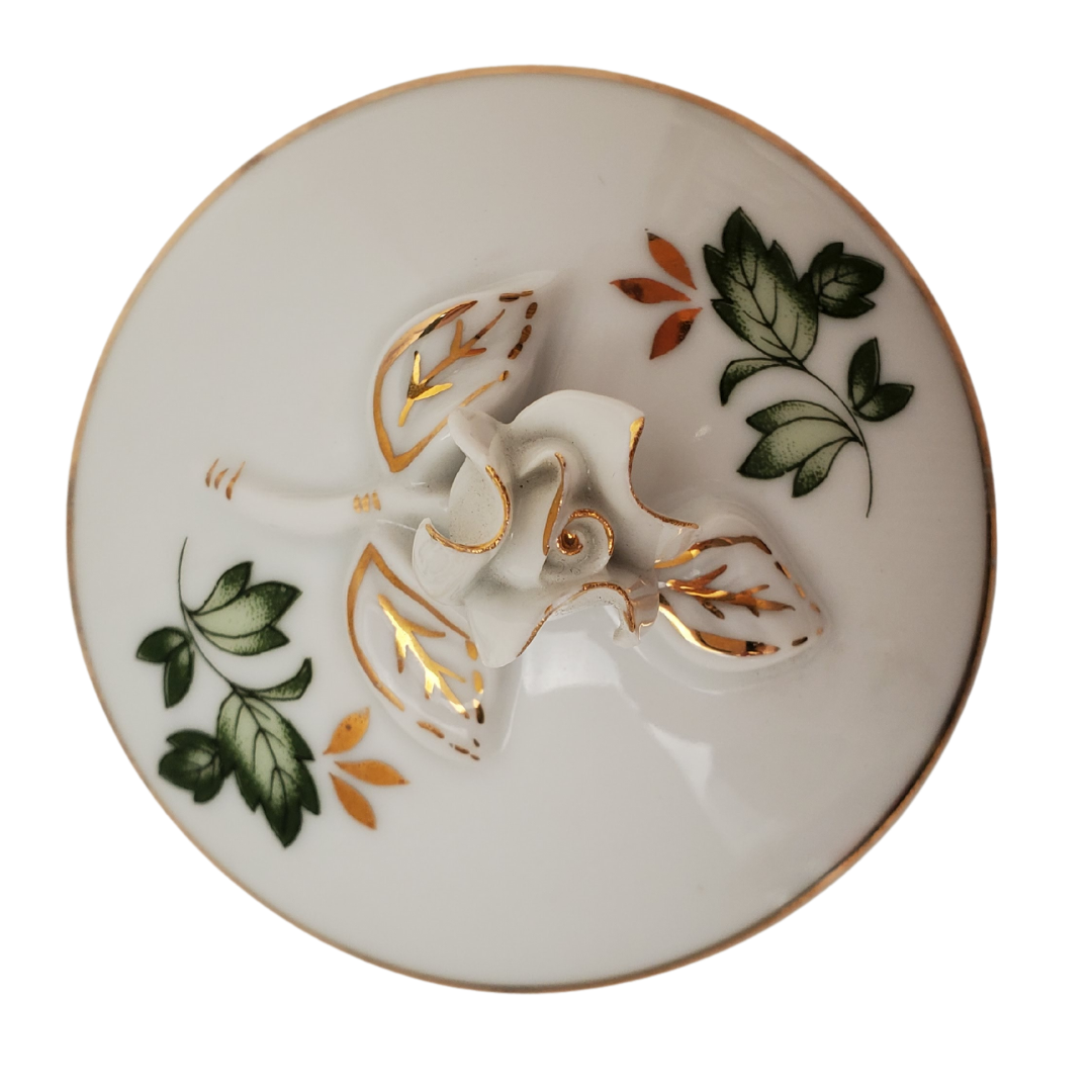 Top View - Pre-owned Hollohaza Hungary porcelain trinket box, with green leaves, gold leaves, gold trimming, and rosebud as handle. Perfect addition to your vanity or bathroom for storing cotton pads!  Measurement: Height: 2.5" Diameter: 2/75"