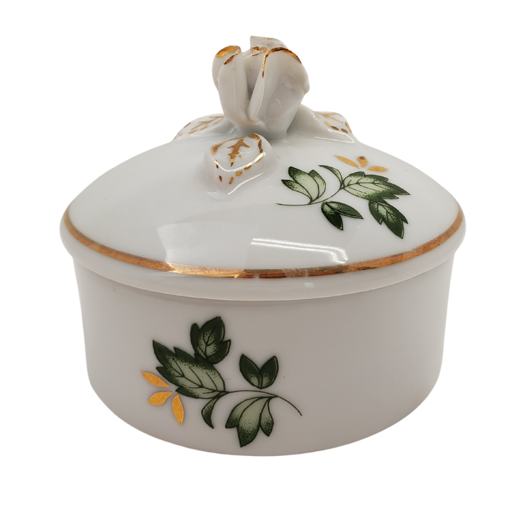 Pre-owned Hollohaza Hungary porcelain trinket box, with green leaves, gold leaves, gold trimming, and rosebud as handle. Perfect addition to your vanity or bathroom for storing cotton pads!  Measurement: Height: 2.5" Diameter: 2/75"